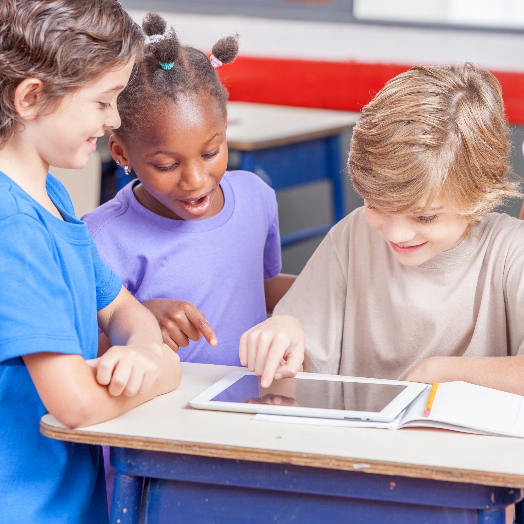 Three children in a classroom, looking at content on a digital tablet.